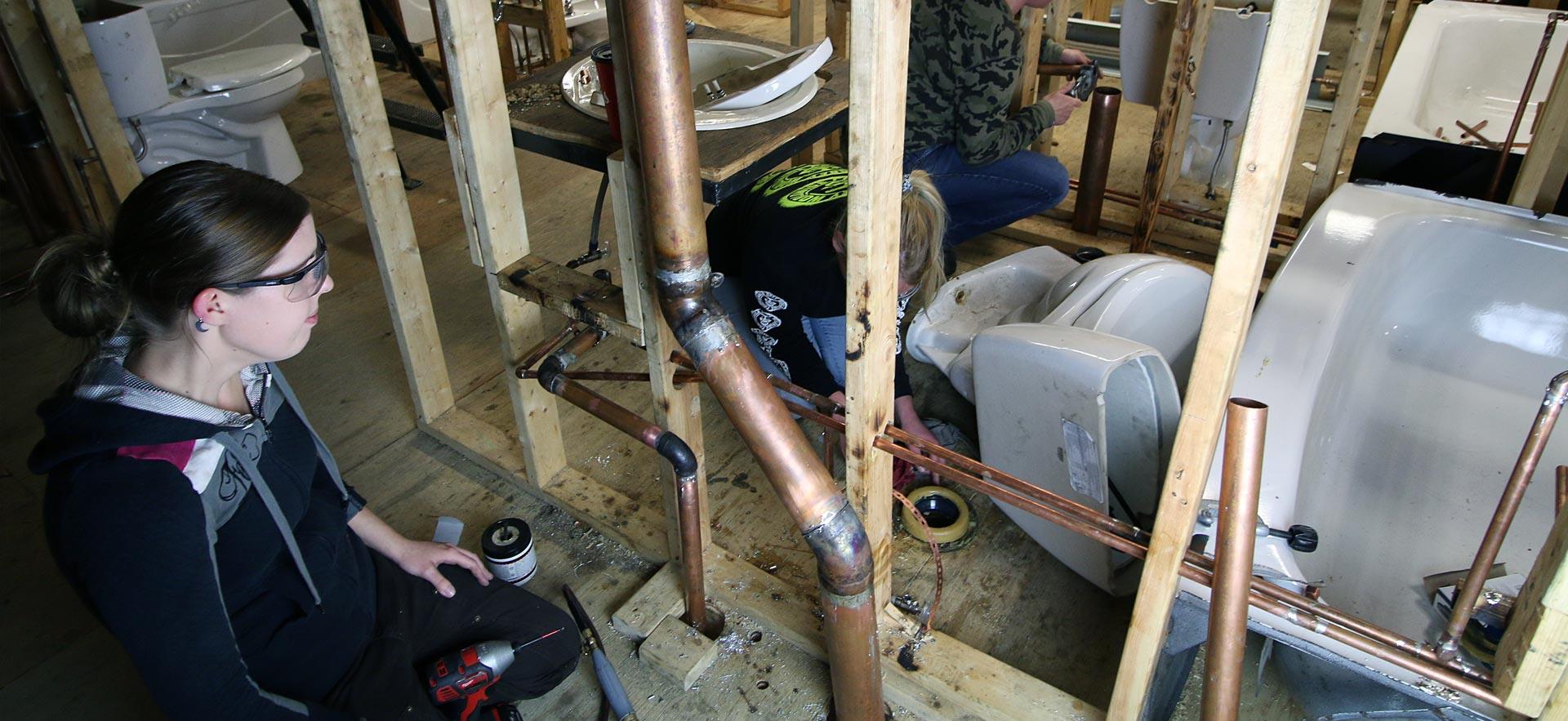 Female plumbing students work on in-class plumbing assignment as ӣƵ. 