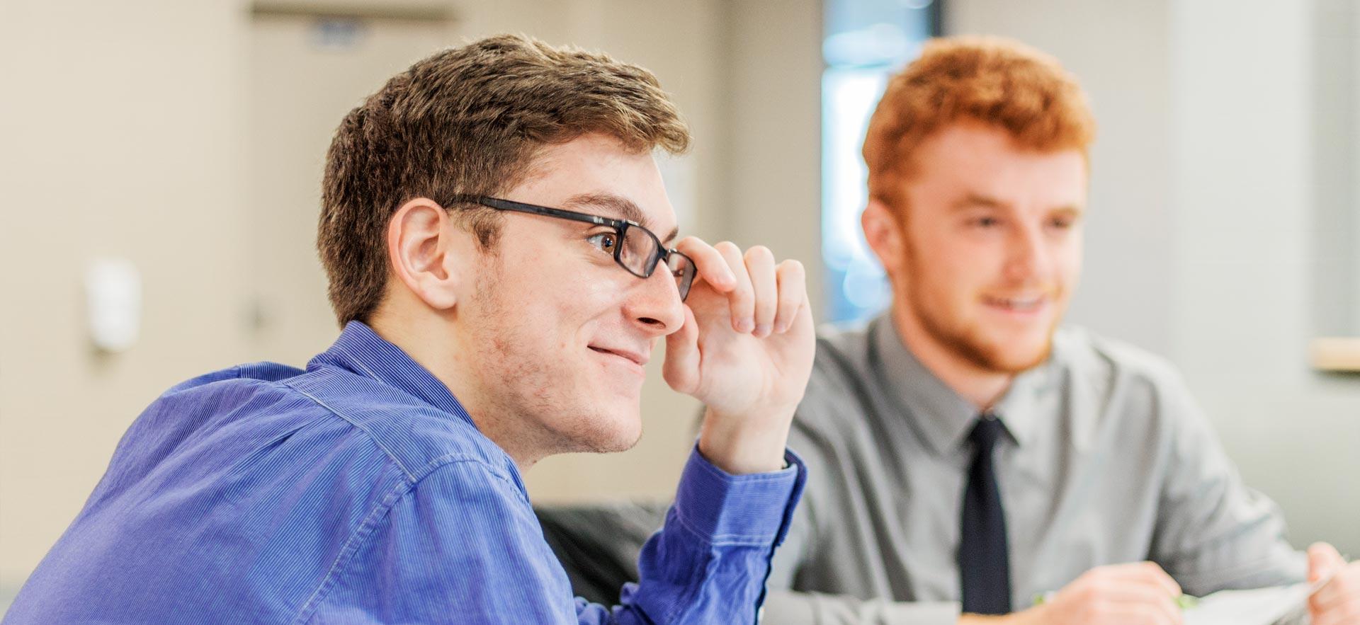 ӣƵ business student smiles and touches his glasses as he listens to his instructor. 