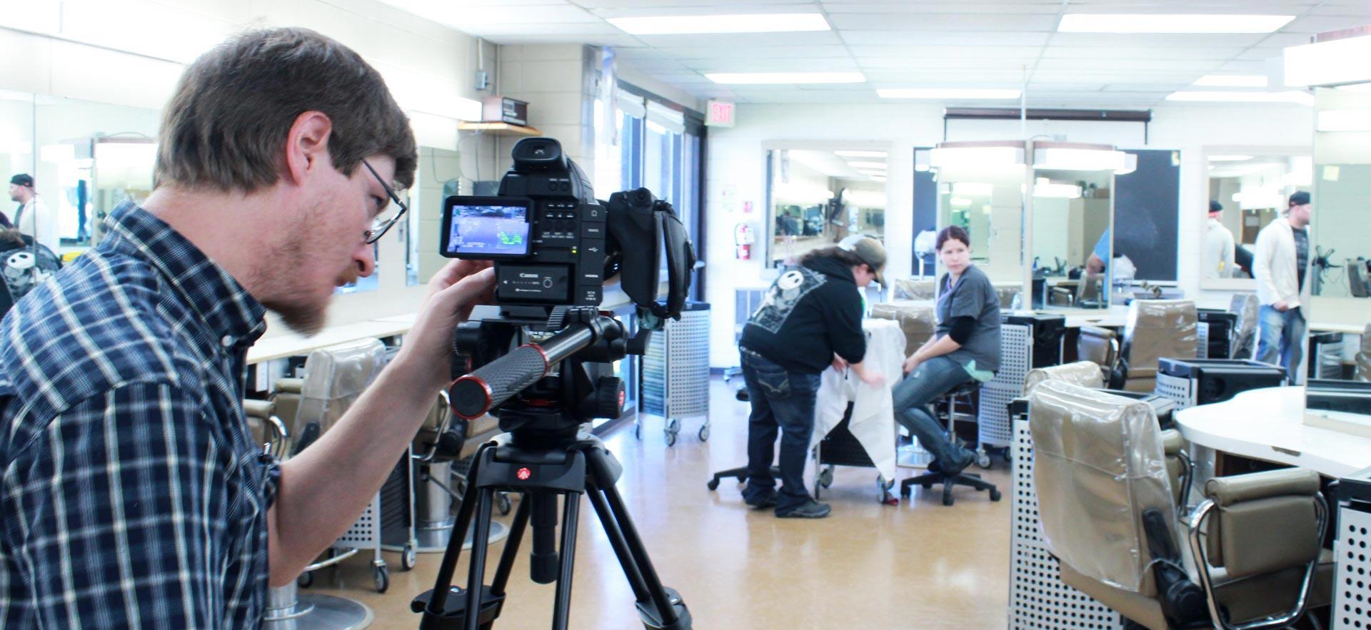 Male digital video student shoots video in the ӣƵ hairstyling salon.
